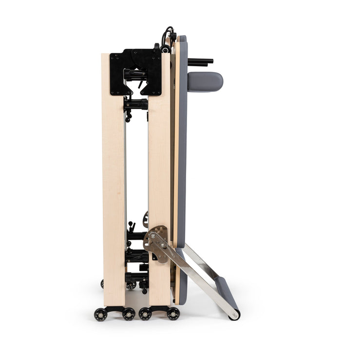 Elina Pilates Fold Reformer folded in half and standing upright on its wheels with grey upholstery