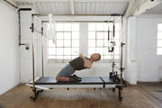Align Pilates Full Cadillac Frame, man kneeling and pulling the upper bar in a studio