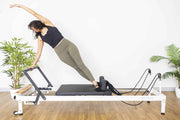 Align Pilates R8-Pro Reformer, woman doing a side stretch on the white frame