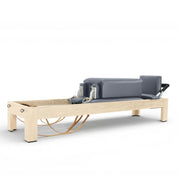 Elina Pilates Classic Natural Wood Reformer in grey with sitting box, leather straps, angled studio view